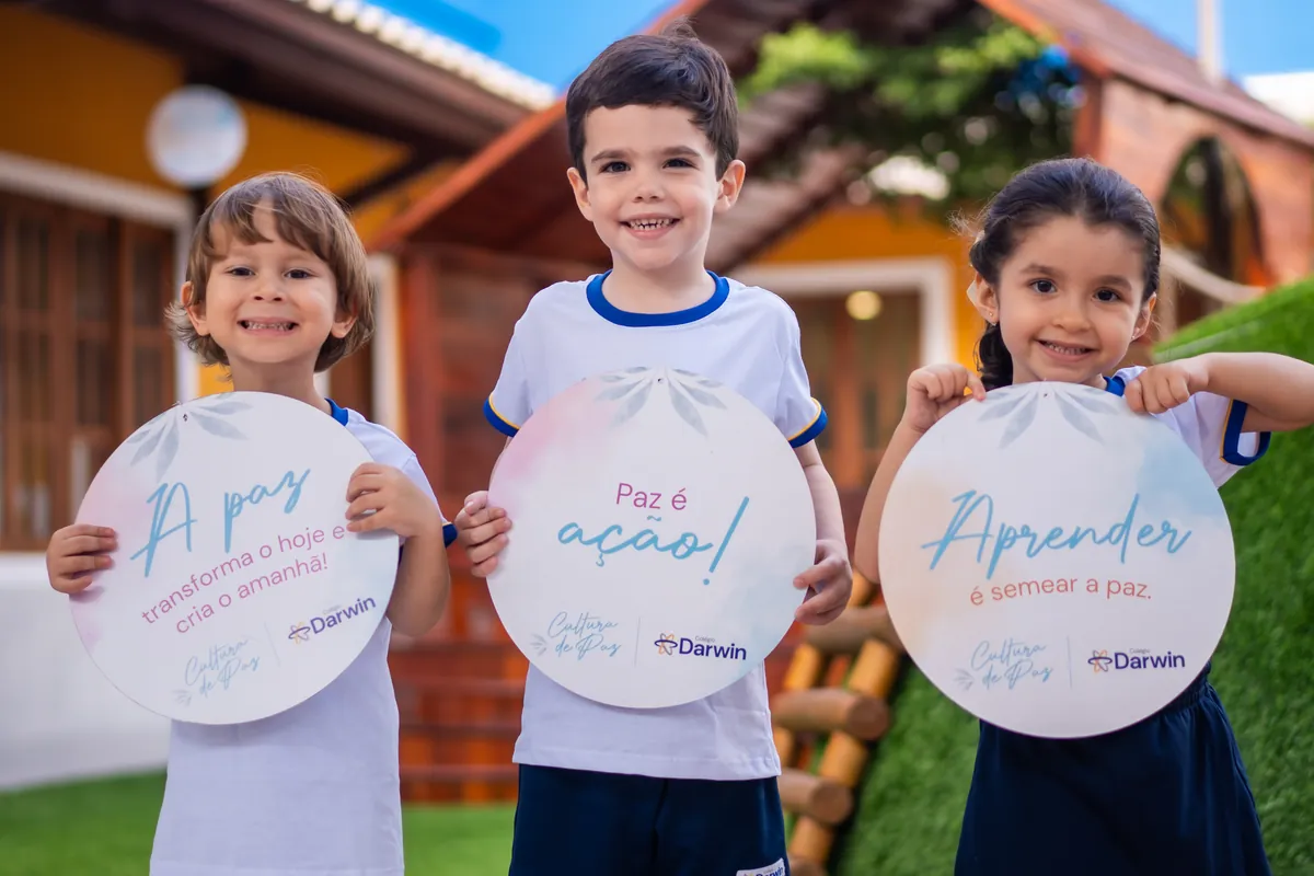 Três crianças do Darwin Infantil segurando plaquinhas com mensagens da Cultura de Paz.