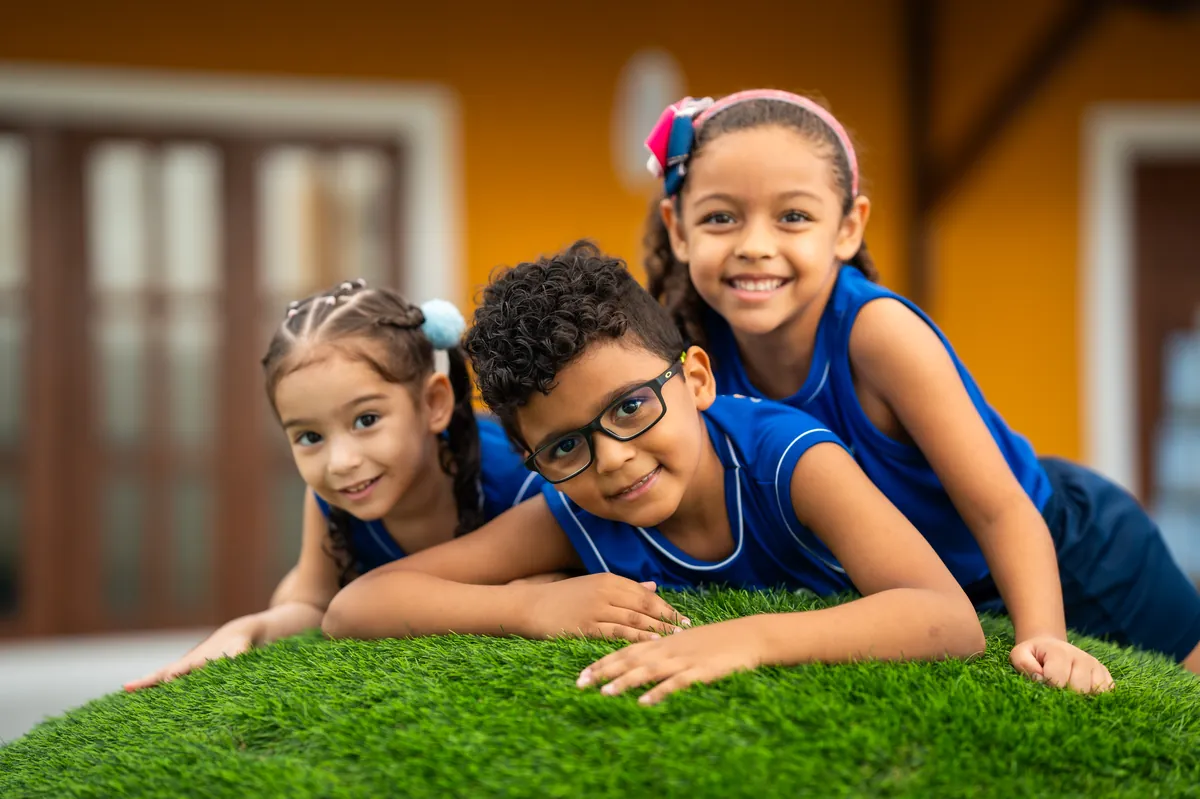 Três alunos do Colégio Darwin deitados na grama, sorrindo para a câmera