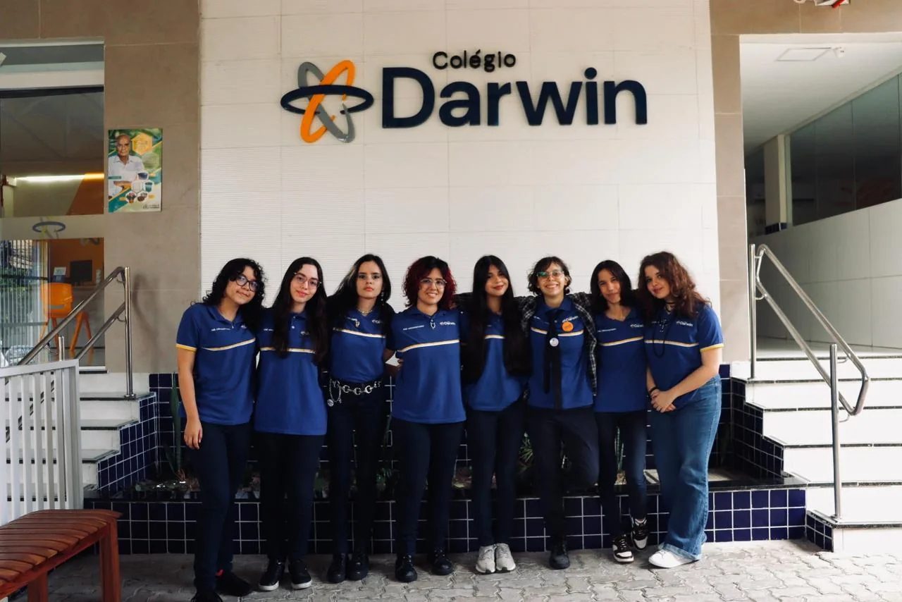 Alunas do Ensino Médio do Colégio Darwin reunidas na escada, sob o letreiro do colégio.